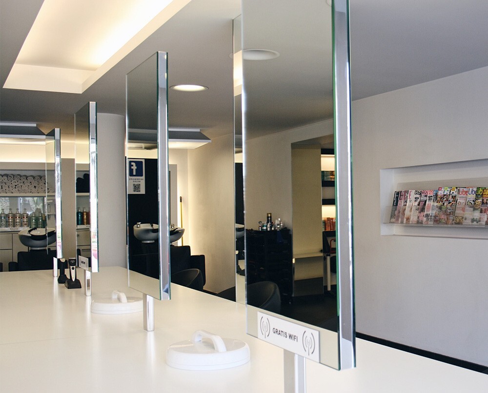 Moderne kappersruimte met spiegels, een witte tafel, en een magazinerek aan de muur.