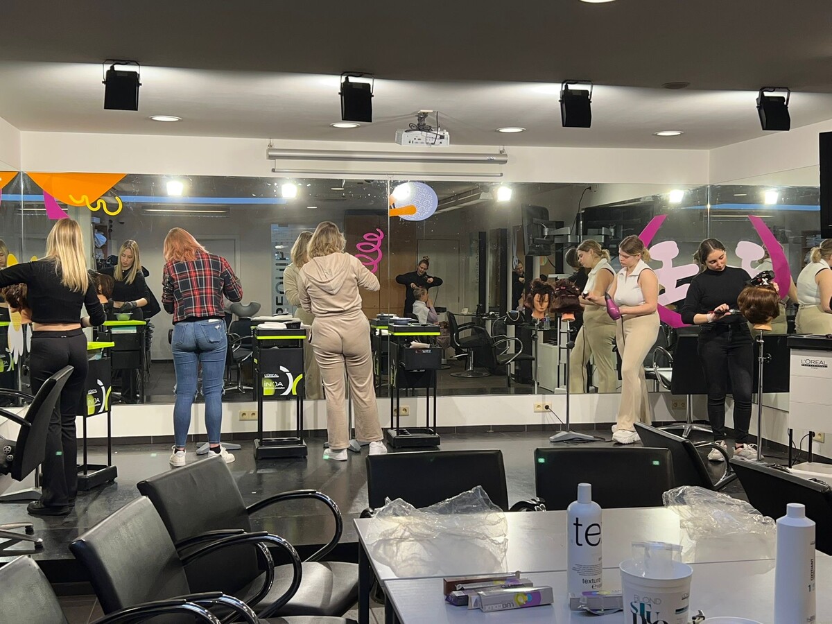 Een groep haarstylisten in een salon die opleiding volgt, met een spiegel aan de muur en diverse kappersbenodigdheden op de tafels.